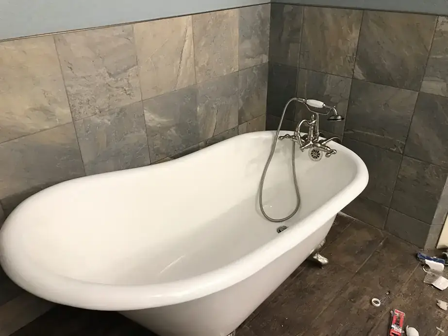 Remodeled bathroom with a white clawfoot tub and telephone faucet against large slate-look tile