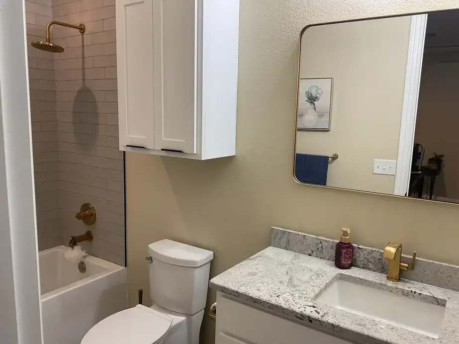 Finished bathroom with brushed gold shower and tub fixtures and a white vanity with a granite top
