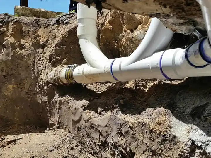 New white PVC wye and couplings tied into an old sewer pipe in an excavation under a house foundation