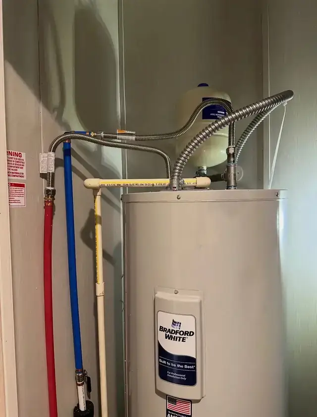 Newly installed tank water heater in a closet with a thermal expansion tank mounted above it
