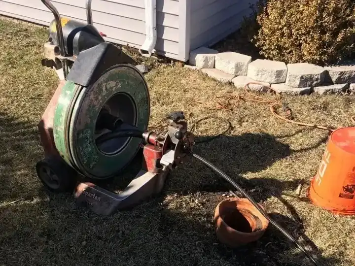 A drum drain machine on a lawn beside a house with its cable running into a clay cleanout