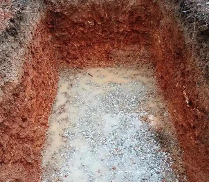 Red clay excavation with a leveled gravel base prepared for a septic tank