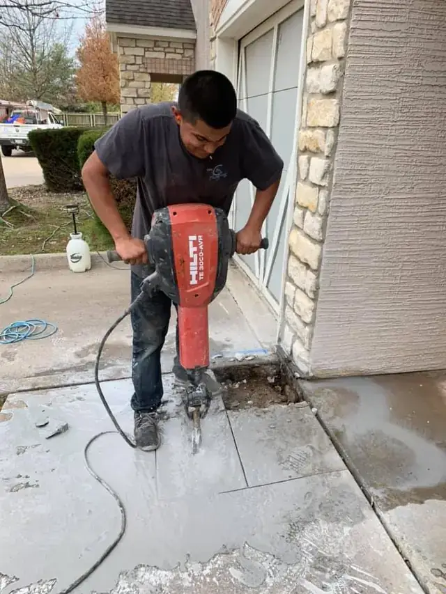 Plumber breaking out a section of concrete with a red breaker hammer to reach a leaking line